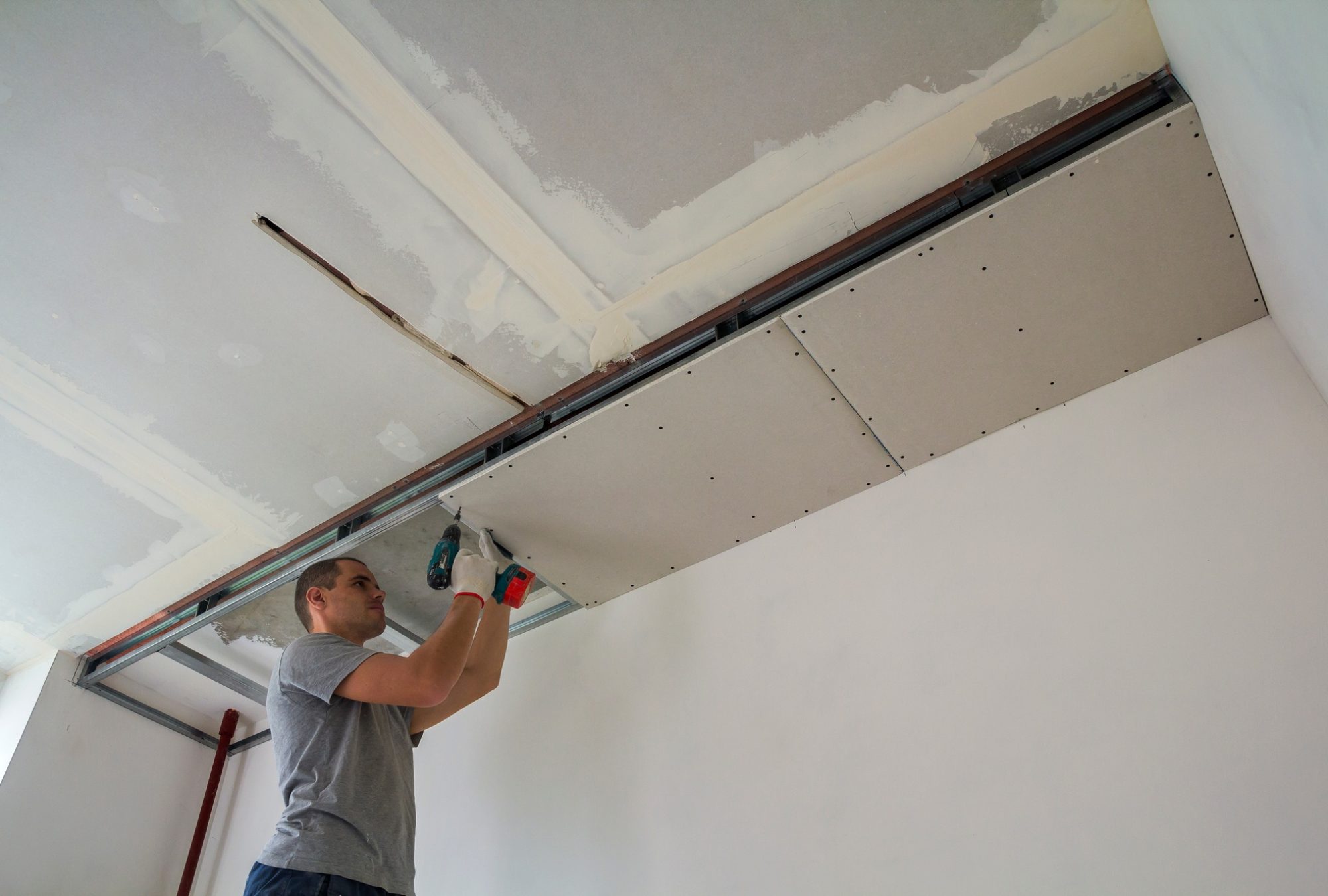 Construction worker assemble a suspended ceiling with drywall and fixing the drywall to the ceiling Construction worker assemble a suspended ceiling with drywall and fixing the drywall to the ceiling